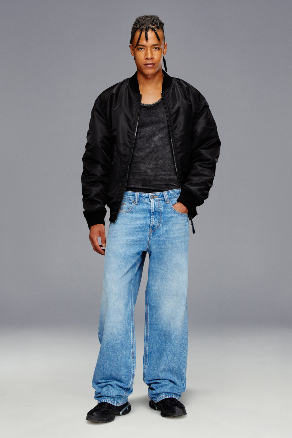 Person wearing a black jacket, black shirt, and blue jeans on a gray background
