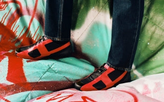 Person wearing blue jeans and red and black sneakers against a graffiti background.