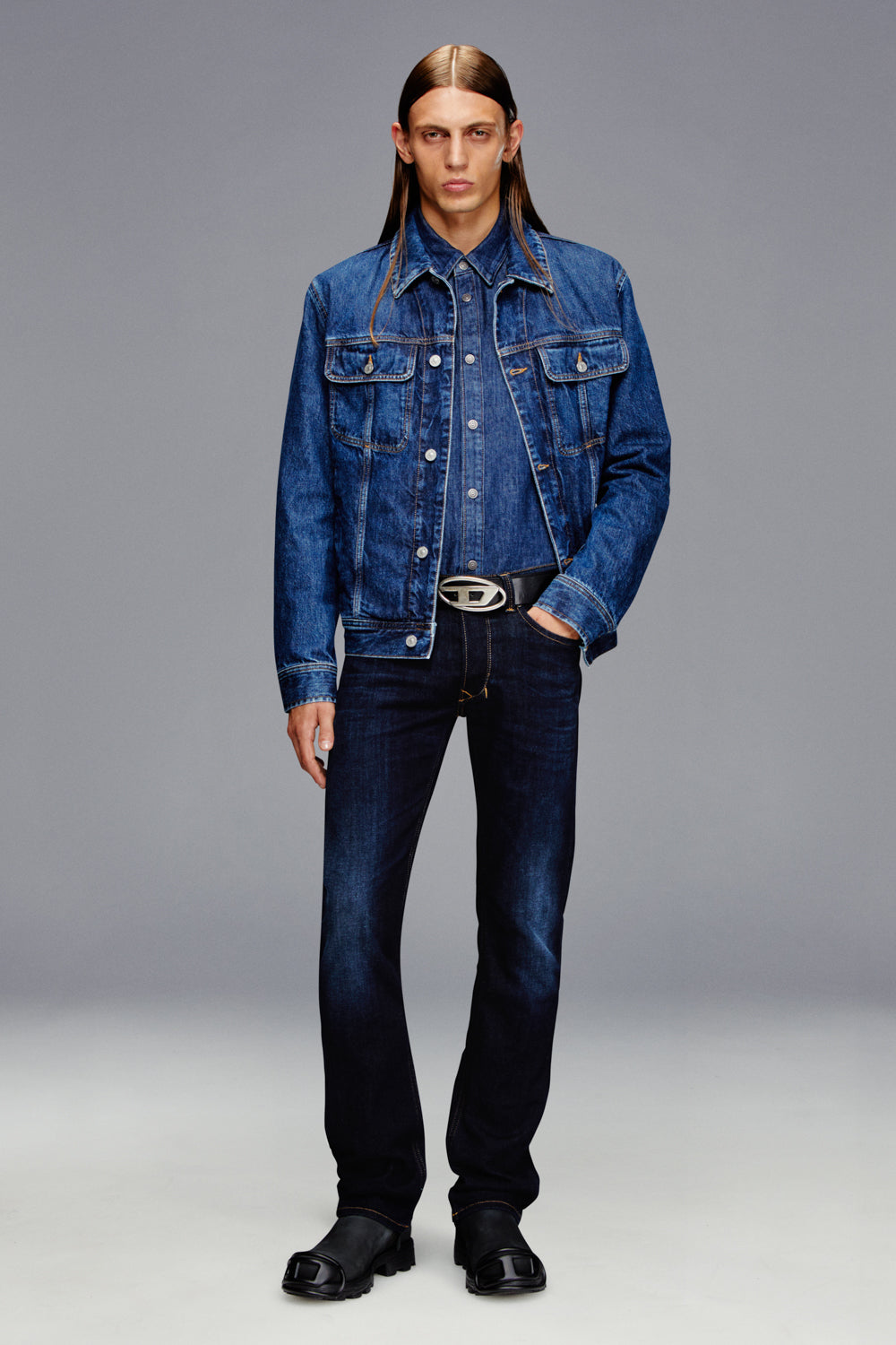 Man wearing a blue denim jacket and jeans on a gray background
