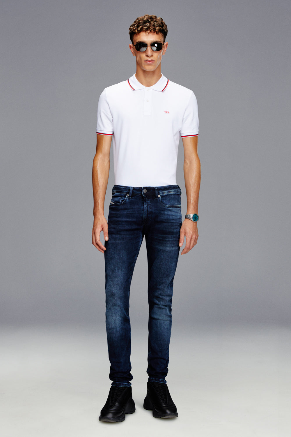 Man wearing a white polo shirt, blue jeans, and black shoes on a gray background