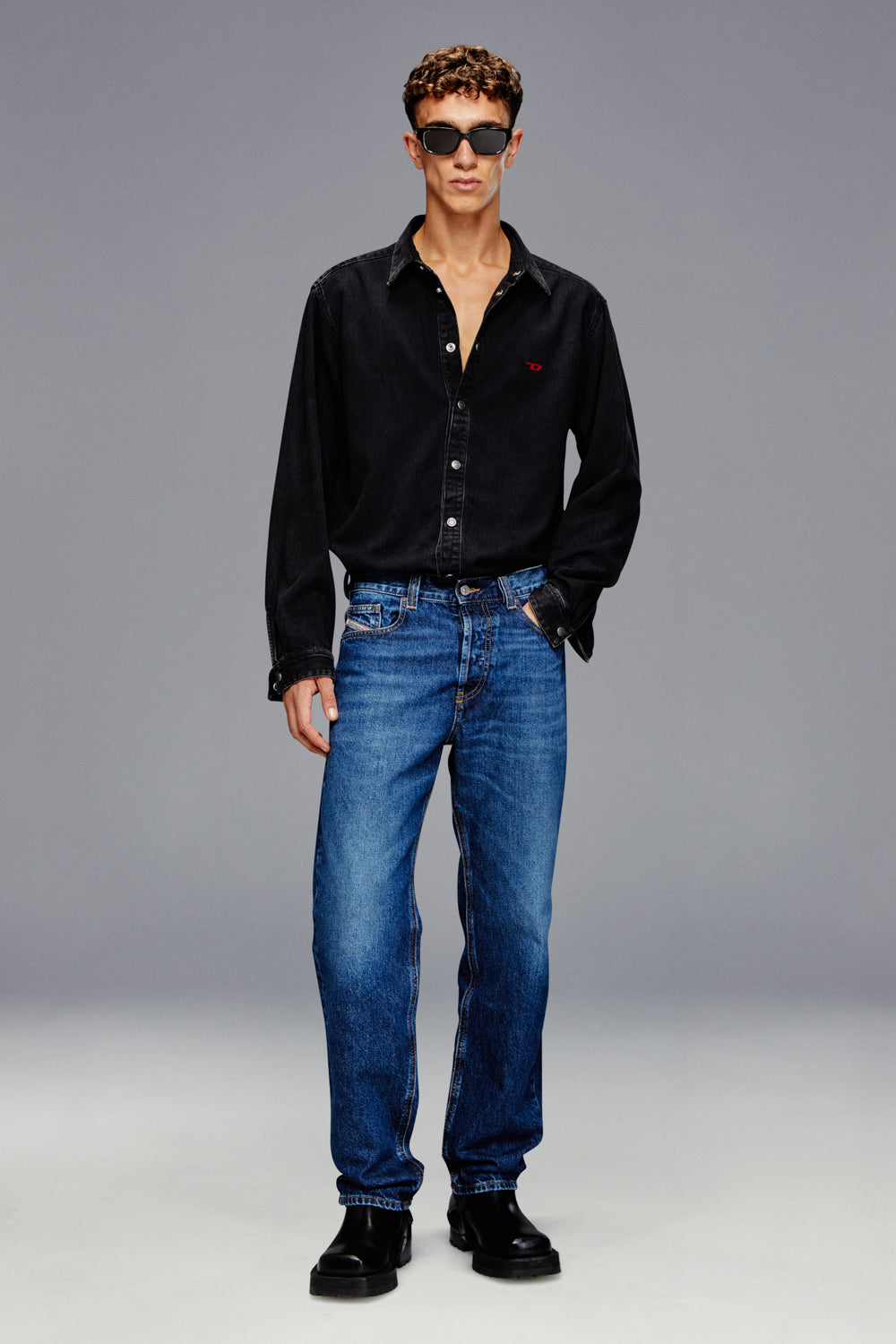 Man wearing a black shirt and blue jeans against a gray background