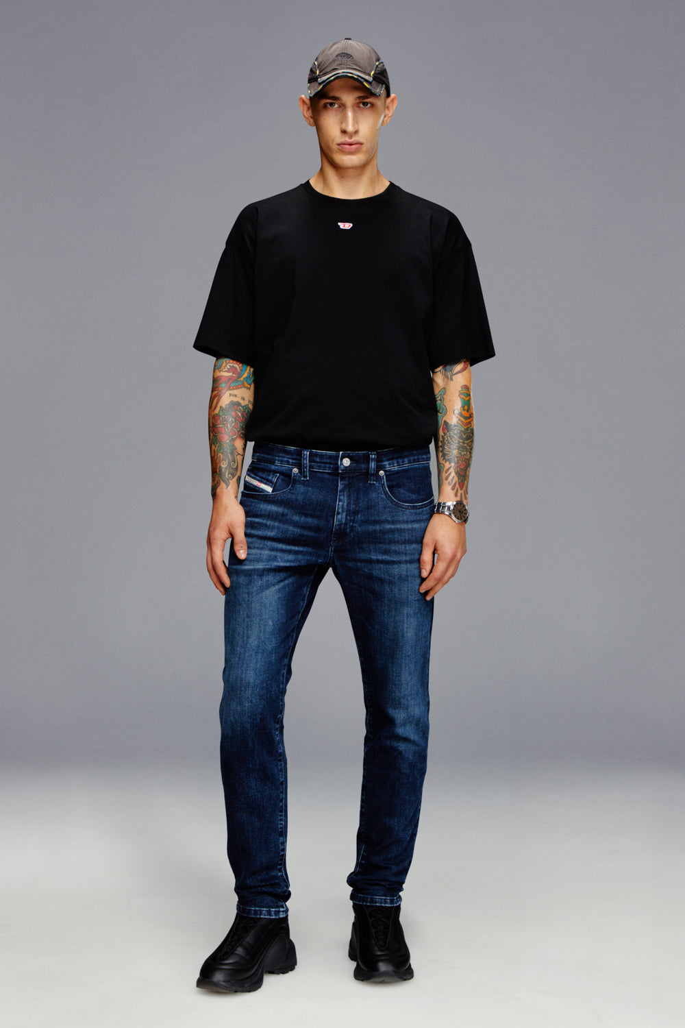 Person wearing a black t-shirt, blue jeans, and a cap on a gray background