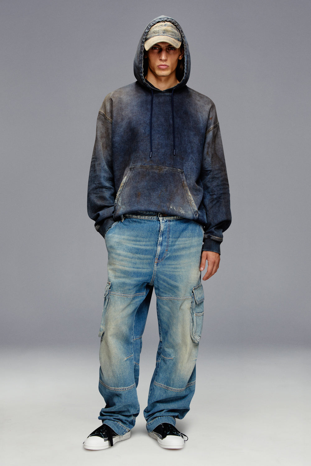 Person wearing a dark hoodie and blue jeans on a gray background