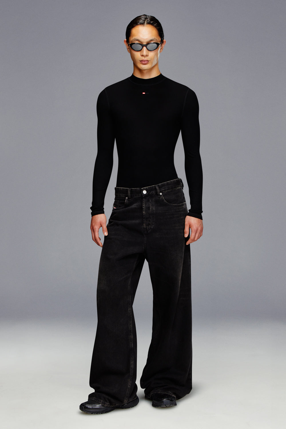 Person wearing a black long-sleeve top and black wide-leg jeans on a gray background
