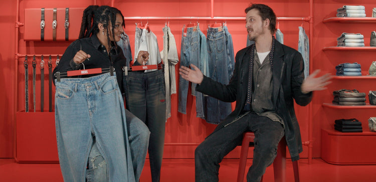 Two people trying on jeans in a store with red walls and clothing racks.